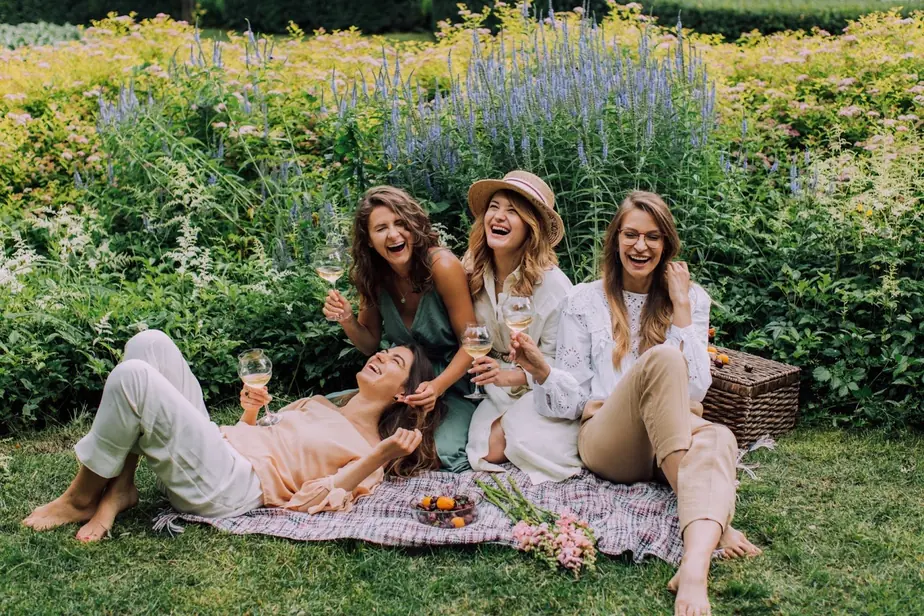 Four friends laughing on a picnic blanket in front of a tall flower border
