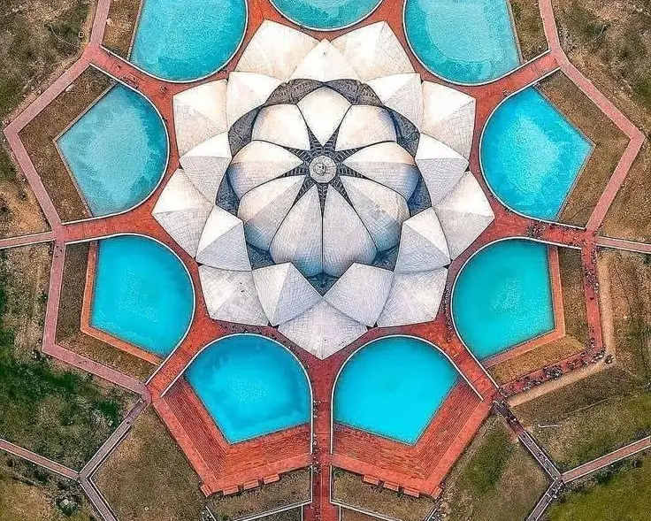 A lotus-shaped building seen from directly above, ringed by nine pools of blue water