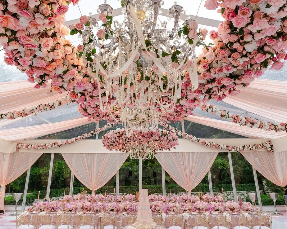A banquet table under a clear-roofed marquee hung with chandeliers and pink roses